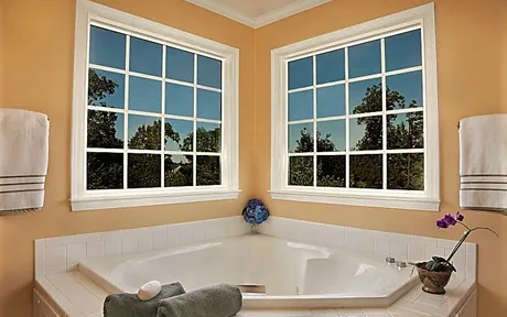 Pair of white vinyl single hung windows with grids above a corner bath